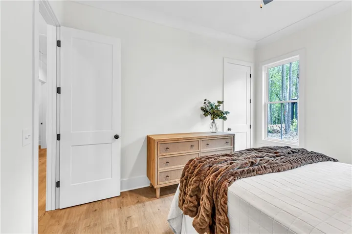 Natural light streams into this bedroom with warm-toned hardwood flooring and crisp white walls.