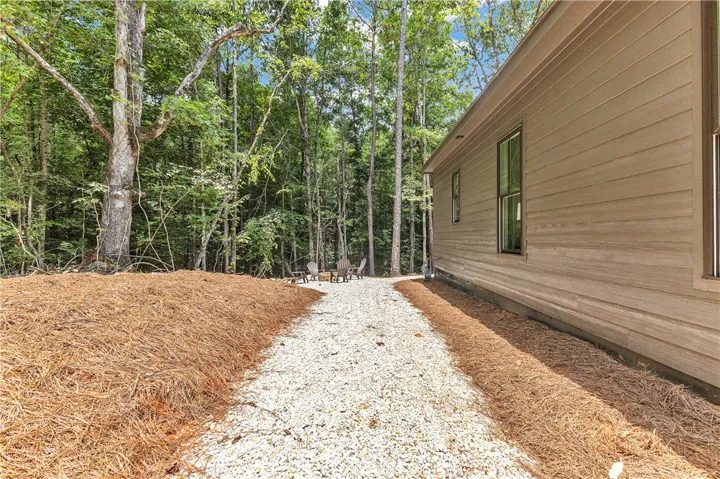 A private gravel path leads to a serene outdoor seating area nestled within lush woodlands.
