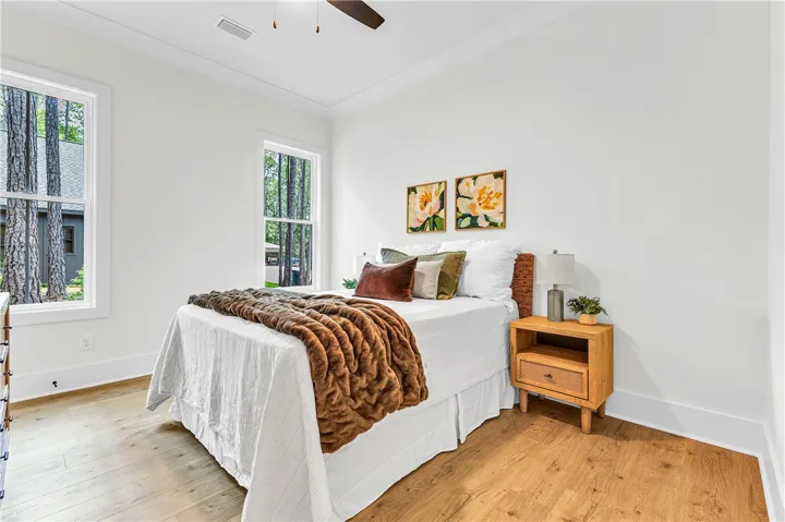 Sun-filled bedroom featuring wide plank hardwood floors and generous windows framing verdant exterior views.