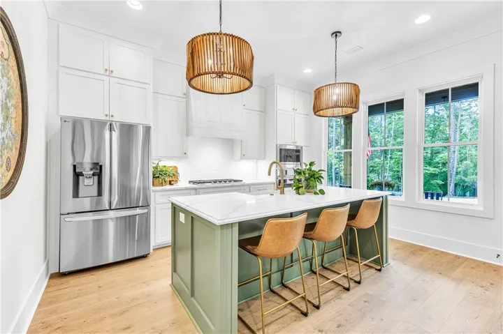A chef's kitchen showcasing a large island with seating and views of abundant greenery.