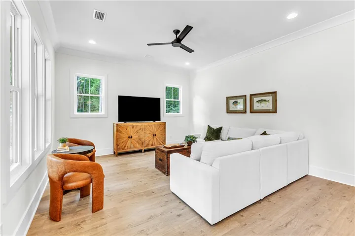 A naturally illuminated living room features a striking ceiling fan and rich hardwood flooring.