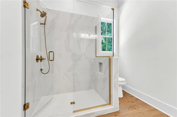 A sleek, walk-in shower features gold-toned fixtures and natural light, complementing the wood-look flooring.