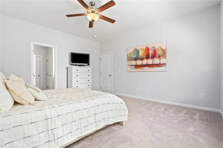 A well-lit bedroom featuring a ceiling fan and plush carpeting throughout.