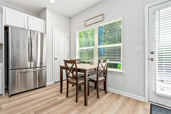 A streamlined kitchen layout features light-toned wooden flooring and a window overlooking lush greenery.