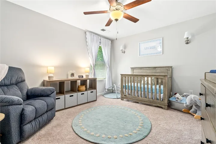 A well-lit nursery features soft carpet and a comfortable rocking chair, creating a serene space for new beginnings.