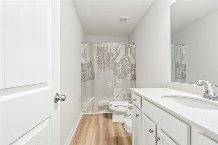 A well-appointed bathroom with durable wood-look flooring and a functional shower-over-tub setup.