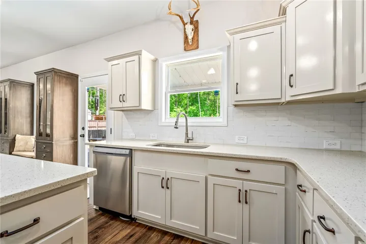 This bright kitchen features white cabinetry and countertops, a stainless steel dishwasher, and rich wood flooring.