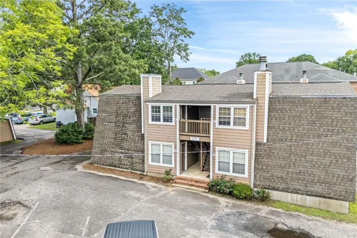A split-level residential building offers private entryways and an upper-level balcony, nestled amidst mature trees.