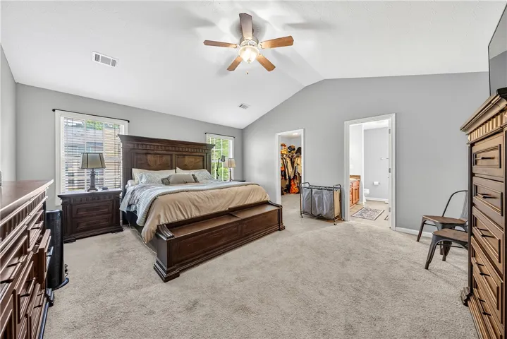 This spacious primary bedroom features soft carpeting, a ceiling fan, and convenient access to a walk-in closet and a private bathroom.