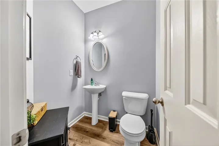 This bright bathroom features hardwood flooring and a classic pedestal sink, offering functional design.