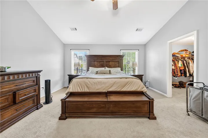 This spacious primary bedroom features soft carpeting and ample natural light from two large windows.