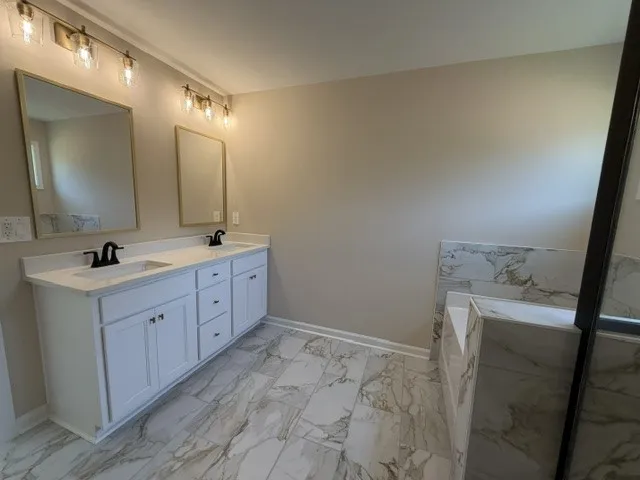 Dual vanities with sleek black fixtures complement the marbled tile flooring in this primary bathroom.