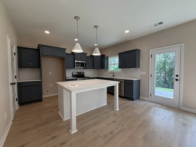 A contemporary kitchen space boasts sleek cabinetry and a central island, complemented by luminous wood flooring.