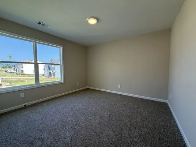 A quiet secondary bedroom offers ample natural light with plush carpeting underfoot.