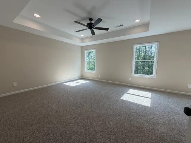 A spacious primary bedroom with a soaring tray ceiling and soft carpeting offers peaceful woodland views.