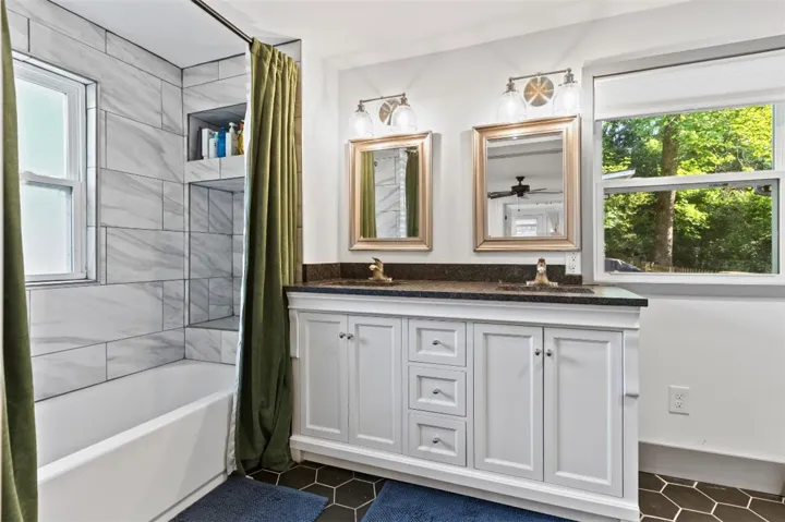 This bright bathroom features a spacious dual vanity and a tub with tiled walls.
