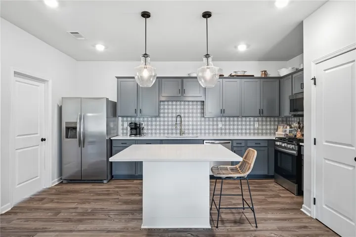 The backsplash brings the fun to this kitchen, complete with quartz counters, grey cabinetry, stainless appliances, and cute pendant lighting.
