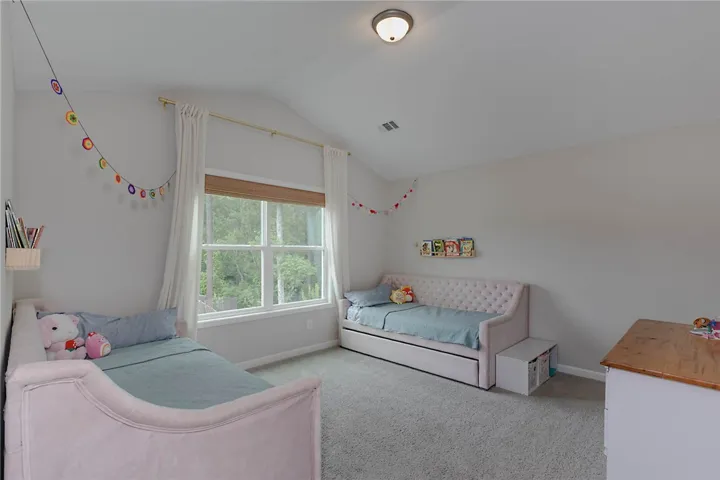 This cozy bedroom features vaulted ceilings and a serene view of lush greenery through large windows.