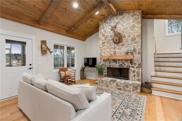 This inviting living area features a grand stone fireplace, exposed beam ceiling, and warm hardwood floors.