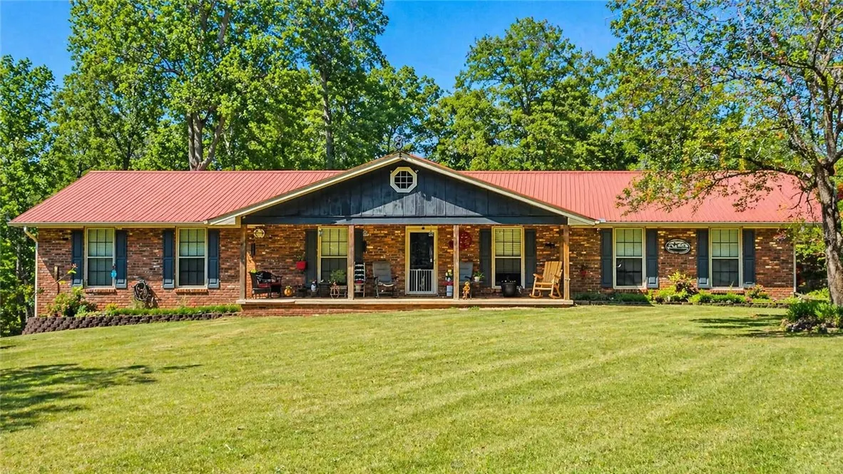 This classic brick residence features a welcoming porch, lush green lawn, and mature trees for privacy.