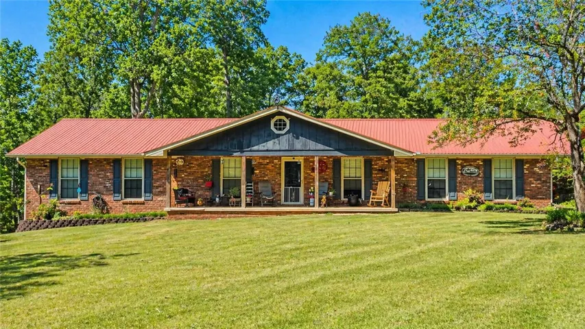 This classic brick residence features a welcoming porch, lush green lawn, and mature trees for privacy.