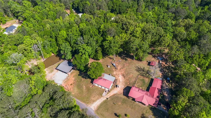 An aerial view showcases a secluded estate amidst lush woodland with multiple structures and a serene pond.