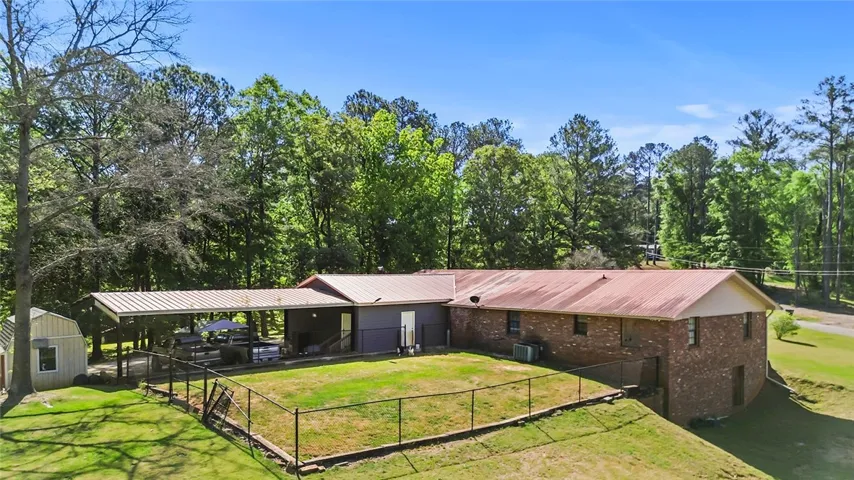 This property features a fenced yard, shed, and carport, all surrounded by lush trees.