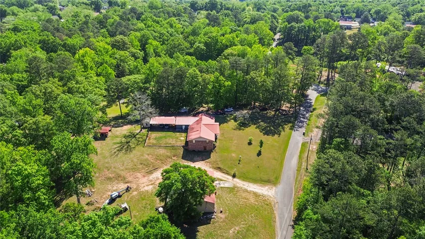 Expansive property surrounded by lush greenery, featuring a main residence and additional structures amidst a private, verdant landscape.