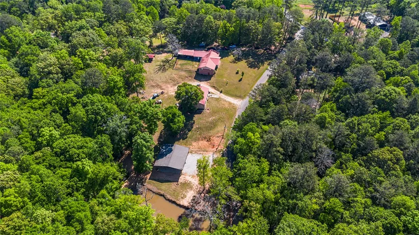 An aerial view captures a spacious estate nestled amidst a vibrant, tree-filled landscape.