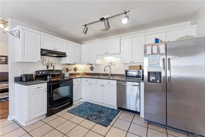 This bright kitchen features white cabinetry, modern appliances, and durable tile flooring.