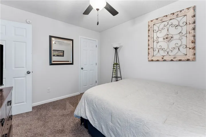 This cozy bedroom features a ceiling fan, plush carpet, and ample natural light.