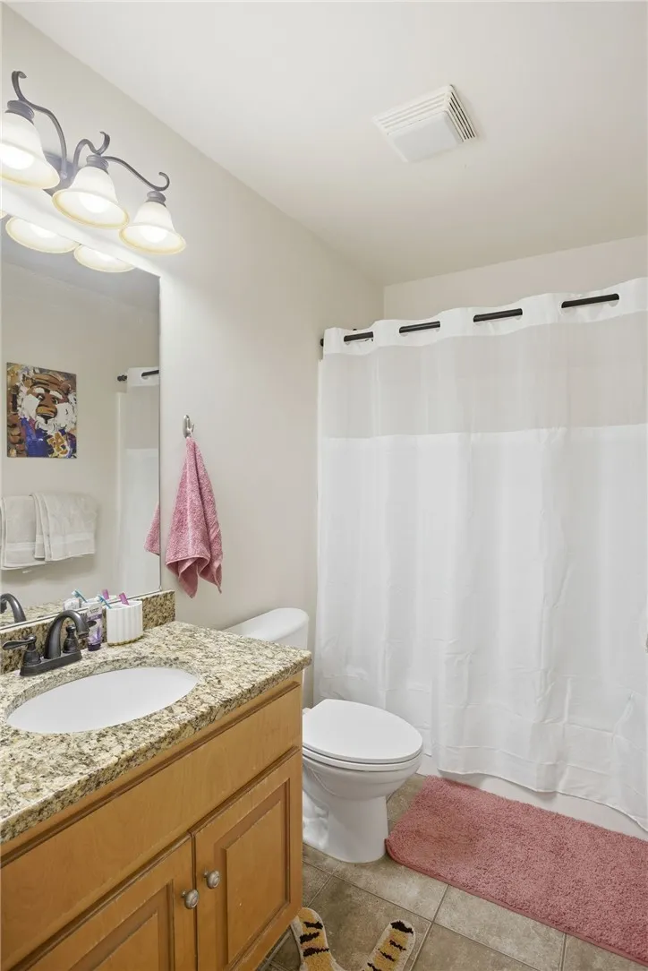 This bright bathroom features a vanity with granite counters and tiled flooring for a clean aesthetic.