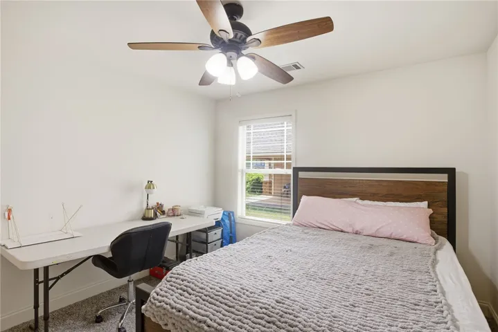 This cozy bedroom features bright walls, carpet flooring, and a large window, offering comfort and natural light.