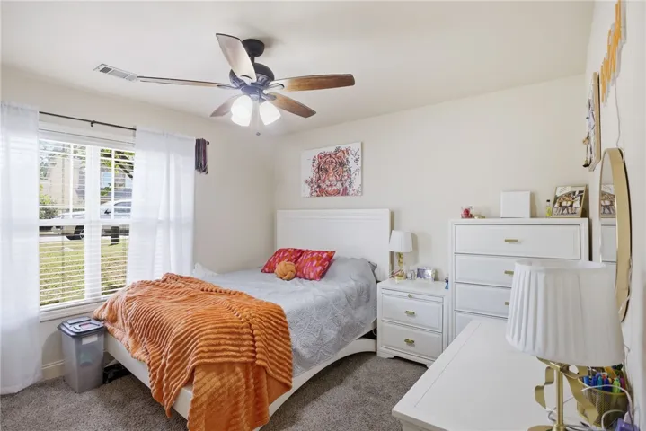 This cozy bedroom features plush carpeting, a large window, and a ceiling fan for ultimate comfort.