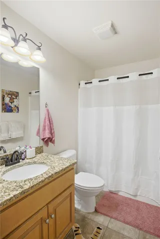 This bright bathroom features a vanity with granite counters and tiled flooring for a clean aesthetic.
