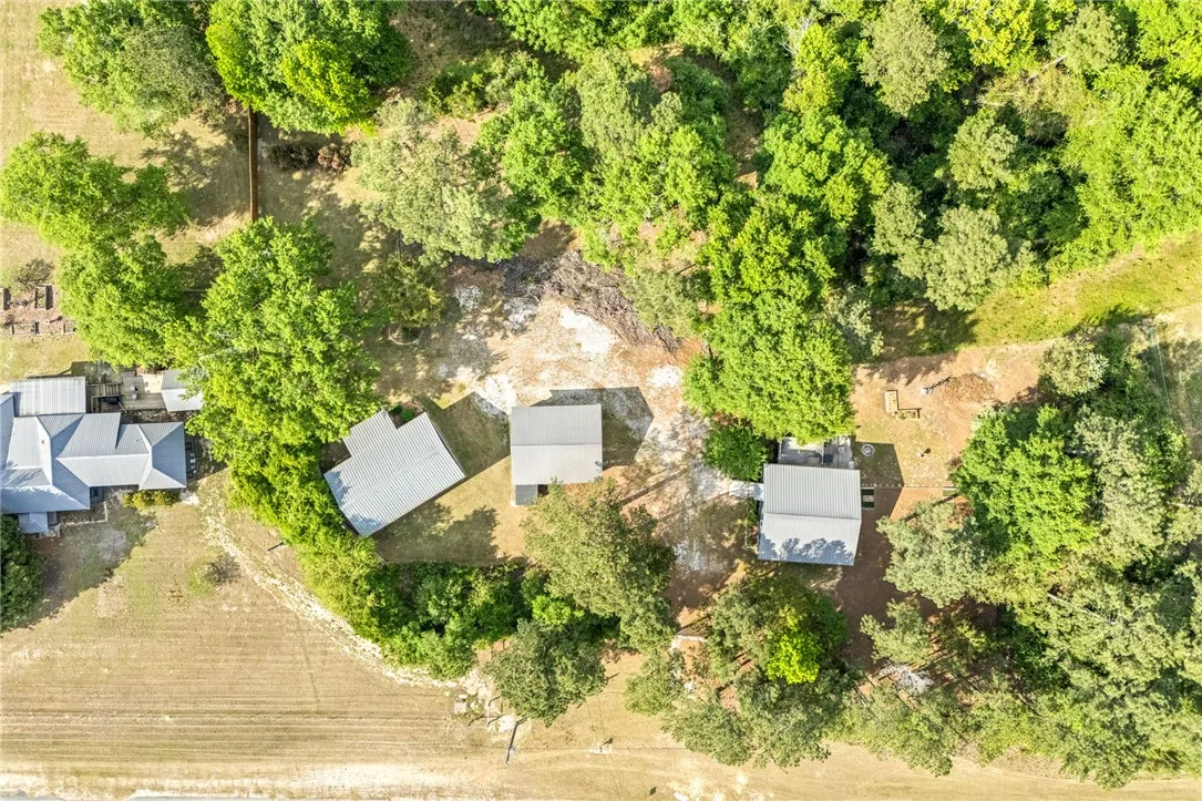 This elevated view showcases a serene, treed parcel featuring multiple structures and open land.