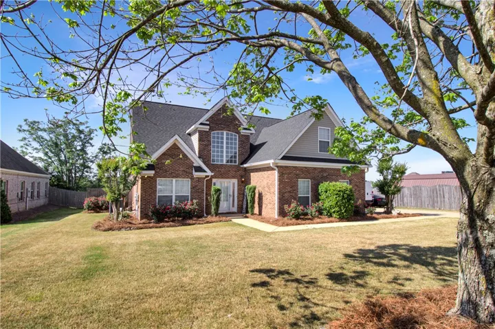 This classic brick residence boasts a neatly manicured lawn and mature landscaping under a clear sky.