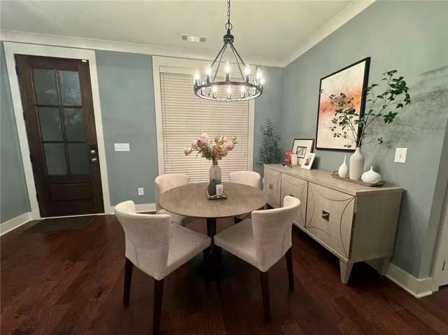 This dining area features rich wood flooring and a modern chandelier, creating an inviting space for gatherings.