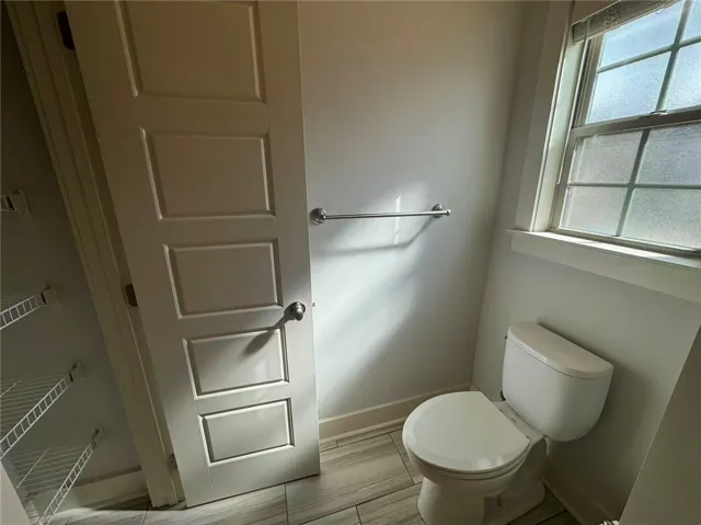 This bright bathroom features a convenient toilet, elegant tile flooring, and a window.