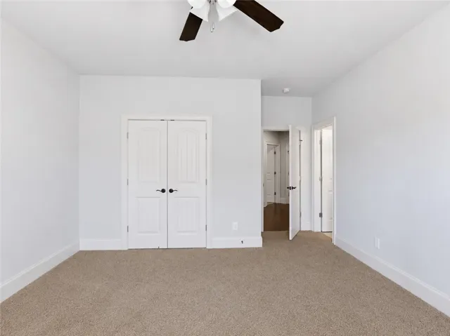 A spacious, naturally illuminated room featuring warm carpet and a functional ceiling fan.