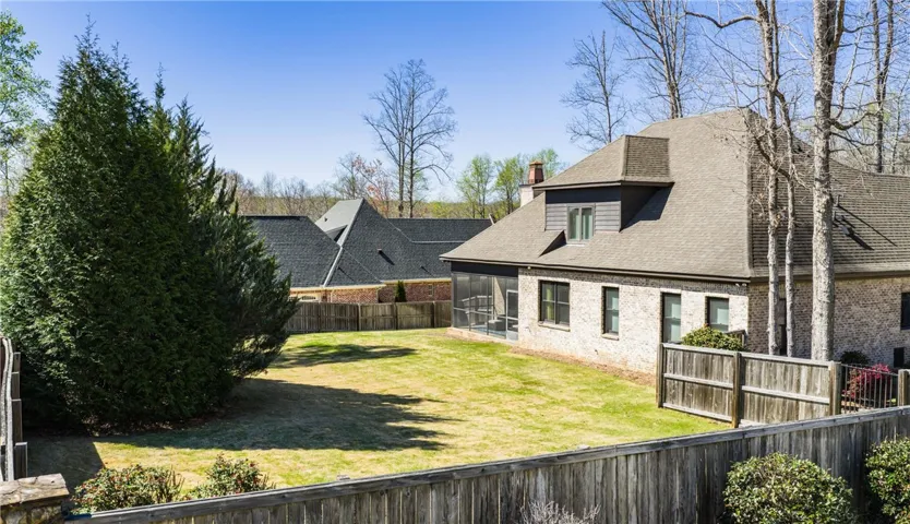 A fenced backyard offers a secure and green space, with a screened porch extending from the home's brick facade.
