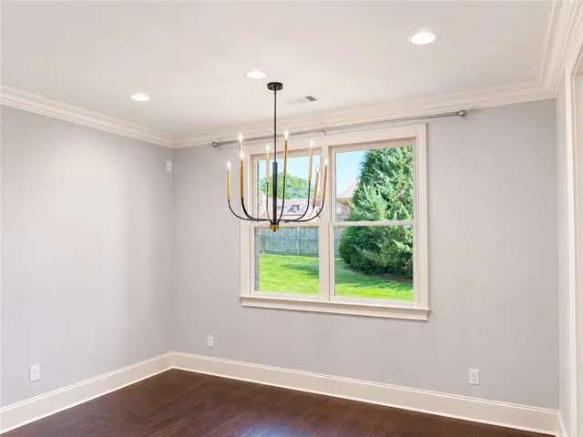 A refined ceiling with crown molding and recessed lighting illuminates rich hardwood floors, framing a window with a pleasant outdoor view.