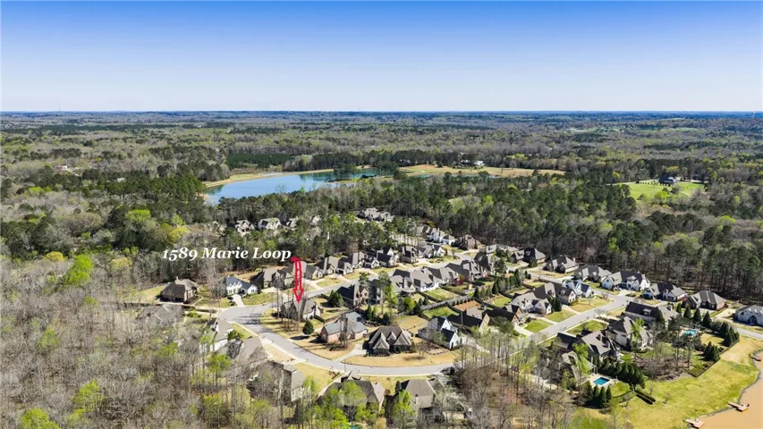 An aerial panorama showcases a serene residential community nestled beside a tranquil lake and verdant woodlands.
