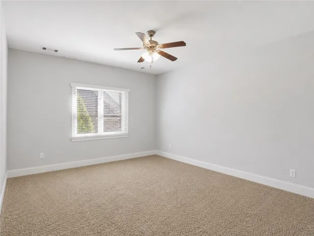 A well-lit bedroom features plush carpeting and a modern ceiling fan, offering a comfortable personal retreat.