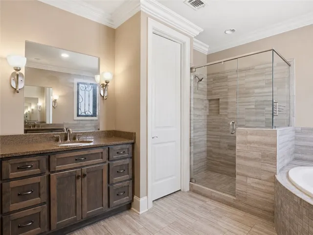 A well-appointed bathroom features a spacious vanity with a broad mirror, glass-enclosed shower, and built-in soaking tub.