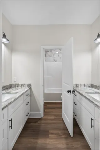 This bathroom features dual vanities with elegant granite countertops and rich hardwood flooring.