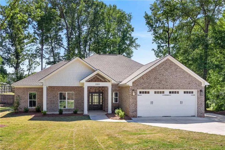 This charming brick residence offers a welcoming facade with an attached garage and mature trees.