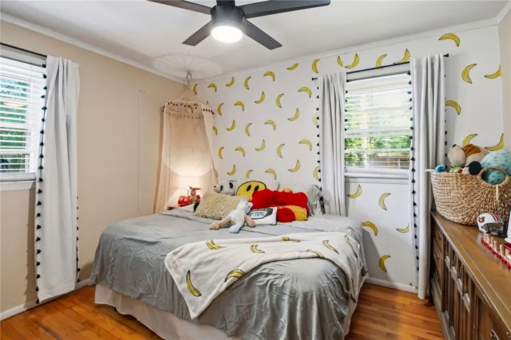 This cozy bedroom features warm wood flooring and a refreshing ceiling fan for comfort.