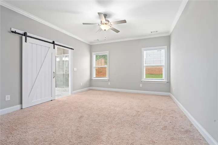 A spacious primary bedroom featuring a barn door entry to the ensuite bathroom and twin naturally illuminated windows.