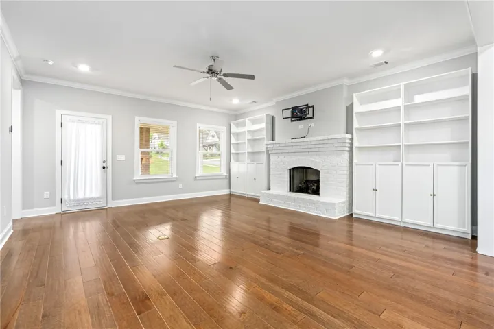 Hardwood floors stretch across this living space, featuring a classic brick fireplace and elegant built-in shelving.